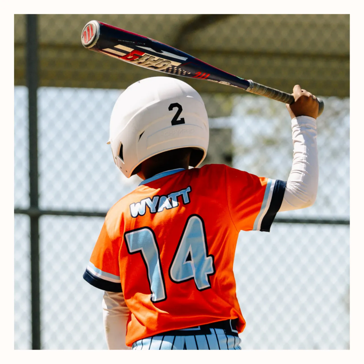 A youth baseball player at bat, photographed from behind during a game.